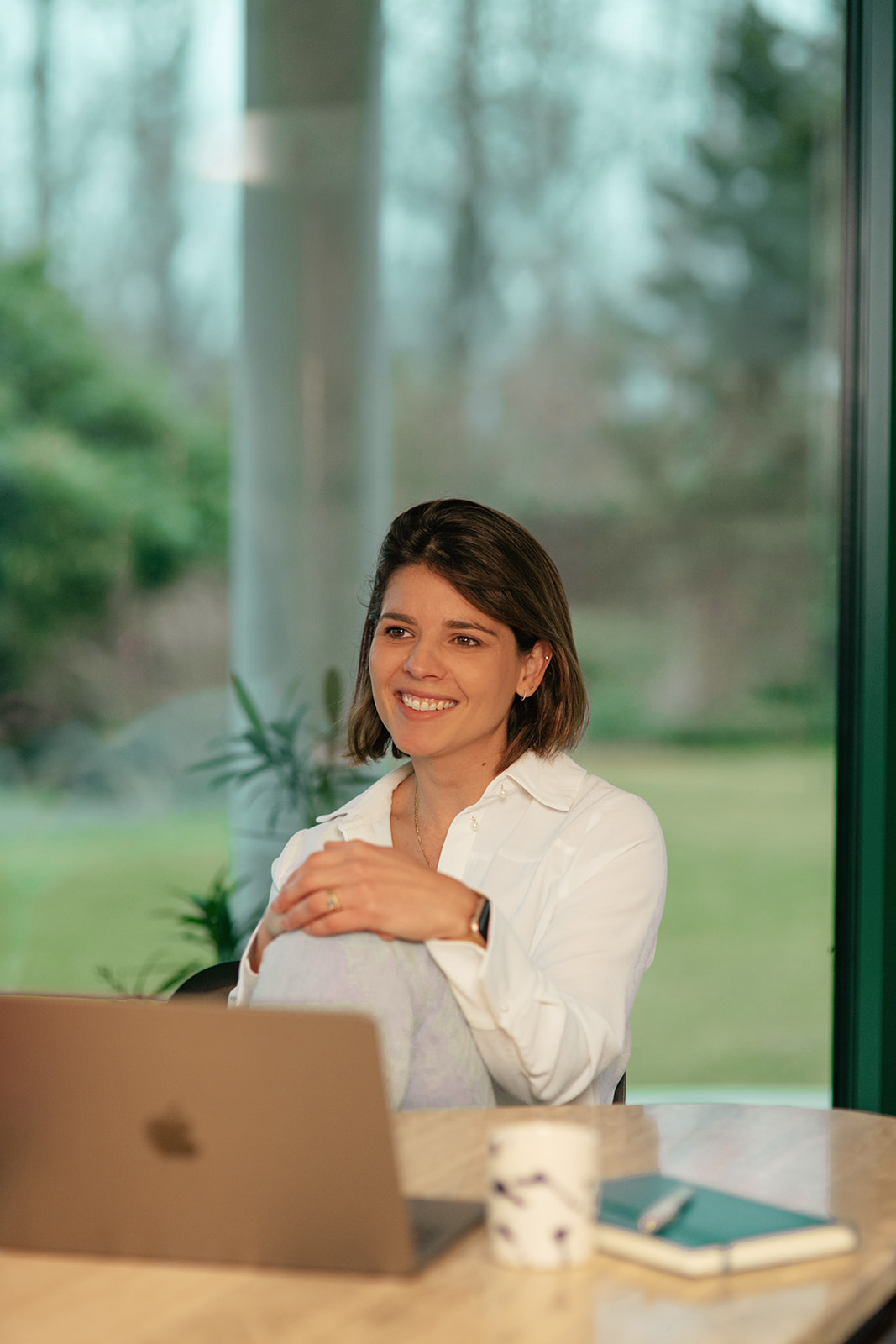 Liselotte aan tafel met laptop, met groene tuin op de achtergrond